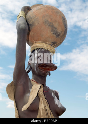 Eine Mursi-Frau trägt eine großen Ton Lippe Platte und Ohr Schmuck entsprechend trägt einen großen Tontopf auf dem Kopf. Stockfoto
