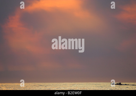 Seenlandschaft in der Abenddämmerung mit Silhouette einsamer Fischerboot und dramatischer Himmel Stockfoto