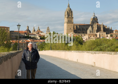 Spanien Salamanca älterer spanischer Mann Spaziergang über römische Brücke über den Rio Tormes mit alten und neuen Kathedrale im Hintergrund Stockfoto