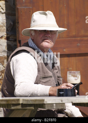 Graue Greis, einen Hut und ein Bier in der Hand hält mit Blick auf die Kamera mit einem sauren Ausdruck. Stockfoto