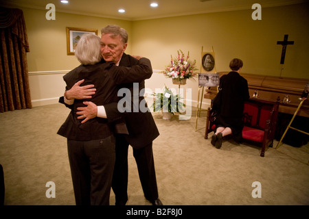Eine Tochter und einen Neffen der verstorbenen Umarmung bei einer Totenwache gehalten bei einem Bestattungsunternehmen in Stoneham MA, wie ein anderer Gast am Sarg kniet Stockfoto