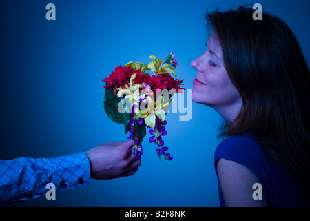 Frau riechen die Blüten angeboten, um sie von einem Mann s ausgestreckten arm Modell veröffentlicht Stockfoto