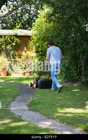 Reifer Mann, den Rasen zu mähen. Englischer Garten im Sommer. VEREINIGTES KÖNIGREICH. Stockfoto