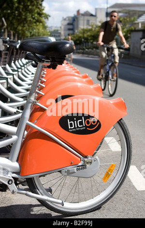 Zeile Bicloo Fahrräder in ihren Docking-Stationen und ein Radfahrer in Nantes, Frankreich (als Velib Fahrräder in Paris) Stockfoto