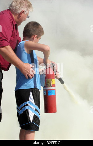 Ein Mann ein Kind zeigt, wie man einen Feuerlöscher verwenden, um ein Feuer auf einem Feuer Sicherheit Messe löschen Stockfoto