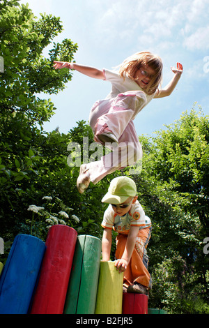 Junge kleine blonde Mädchen Kind springen gerne im Freien aus bunten Stangen am Kinderspielplatz in der Slowakei Stockfoto