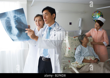 Zwei Ärzte untersuchen einen Röntgen-Bericht eine Krankenschwester mit einem Patienten hinter Ihnen Stockfoto
