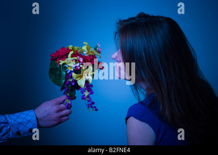 Frau riechen die Blüten angeboten, um sie von einem Mann s ausgestreckten arm Modell veröffentlicht Stockfoto