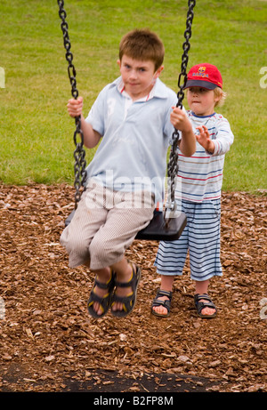 Kleiner Junge schob seinen großen Bruder auf Schaukel im Vereinigten Königreich Stockfoto