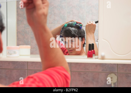 Reife Frau mit Lockenwickler im Badezimmer tun ihr Haar Stockfoto