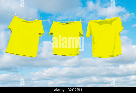 Gelbe Hemden hängen auf einer Wäscheleine vor einem Himmel voller geschwollene weiße Wolken Stockfoto