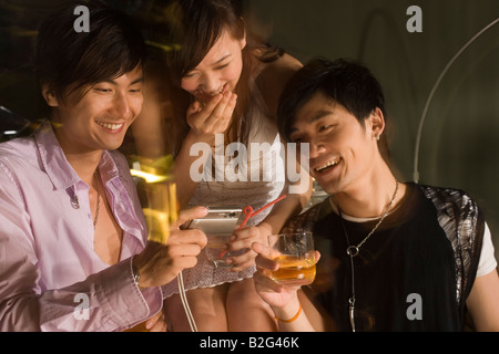 Zwei junge Männer und eine junge Frau mit Blick auf eine digitale Kamera und lächelnd Stockfoto