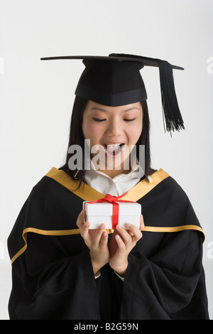 Junge weibliche Absolventen hält ein Geschenk und suchen überrascht Stockfoto