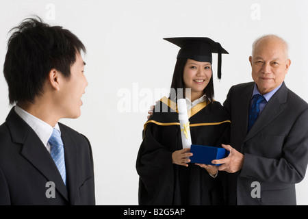 Junge weibliche Absolventin erhält ein Geschenk von ihrem Vater und lächelnd Stockfoto