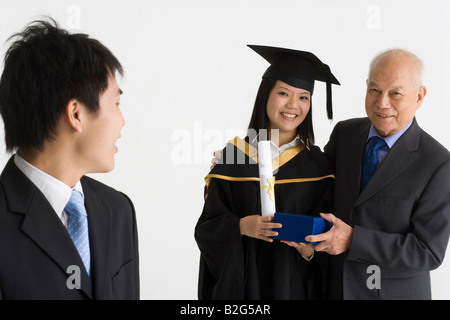 Junge weibliche Absolventin erhält ein Geschenk von ihrem Vater und lächelnd Stockfoto