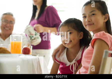 Porträt eines Mädchens mit ihrer Schwester an einem Esstisch sitzen und Lächeln Stockfoto