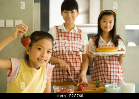 Porträt eines Mädchens mit einer Erdbeere mit ihrer Mutter und Schwester im Hintergrund Stockfoto