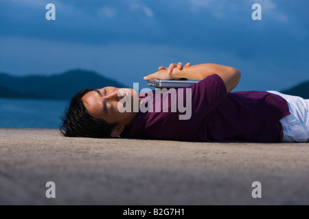 Seitenansicht der Mitte erwachsener Mann mit einem Laptop am Strand liegen Stockfoto