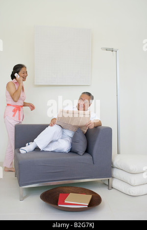 Senior Mann liest eine Zeitung mit einer älteren Frau telefonieren mit einem Handy Stockfoto