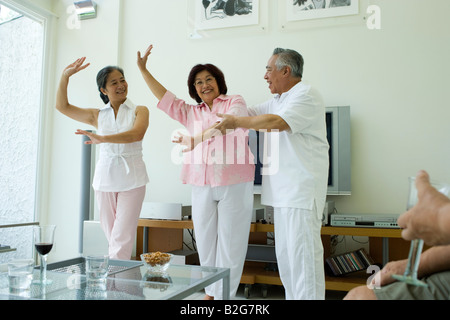 Ältere Mann mit zwei Frauen in Führungspositionen in einem Wohnzimmer tanzen Stockfoto