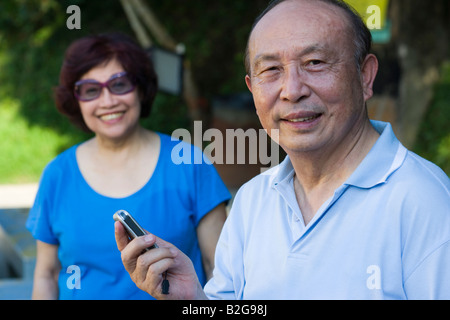 Porträt eines senior ein Handy mit einer reifen Frau lächelnd im Hintergrund halten Stockfoto