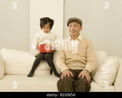 Mädchen hält ein Geschenk und sitzen auf einer Couch mit ihrem Großvater Stockfoto
