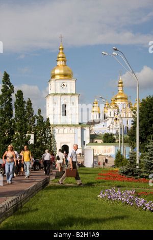 Menschen laufen entlang des Weges zum Kloster St. Michael mit goldener Kuppel in Kiew an einem sonnigen Tag, mit goldenen Kuppeln und üppigem Grün. Stockfoto