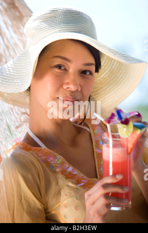 Porträt einer jungen Frau in einer Hängematte liegend und hält ein Glas Cocktail, Phuket, Thailand Stockfoto