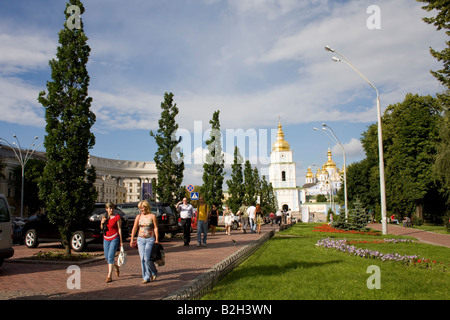 Menschen laufen entlang des Weges zum Kloster St. Michael mit goldener Kuppel in Kiew an einem sonnigen Tag, mit goldenen Kuppeln und üppigem Grün. Stockfoto
