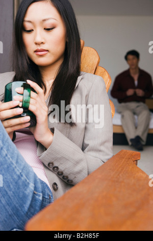 Nahaufnahme einer jungen Frau auf einem Stuhl sitzend, mit einem jungen Mann im Hintergrund Stockfoto