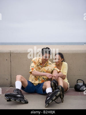 Junges Paar sitzt am Boden und setzen auf Schlittschuhen, Huntington Beach, Kalifornien, USA Stockfoto