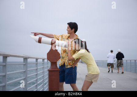 Junge Frau, die durch einen Münz-Fernglas und junger Mann stand neben ihr, Huntington Beach, Kalifornien, USA Stockfoto