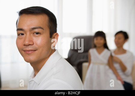 Porträt eines Mitte erwachsenen Mannes lächelnd mit seiner Frau und seiner Tochter im Hintergrund, Singapur Stockfoto