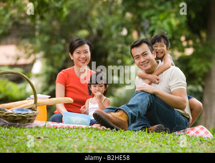 Porträt eines Mitte Erwachsenen Paares mit ihren beiden Töchtern mit Picknick in einem Park, Singapur Stockfoto