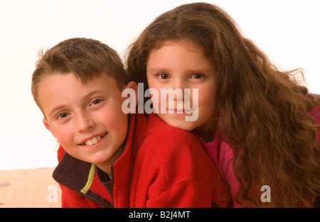 Weibliches Kind mit langen Haaren auf dem Rücken eines männlichen Kindes auf einem Holzboden. Weißer Hintergrund. Stockfoto