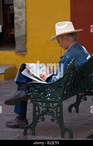 Eine mexikanische Mann liest Zeitung auf einer Stadt-Bank im historischen GUANAJUATO Mexiko Stockfoto