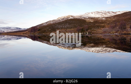 Die Wintermorgen strahlend blauer Himmel und schneebedeckte Berge spiegeln sich in den ruhigen Gewässern des Loch Tarff, Schottisches Hochland Stockfoto