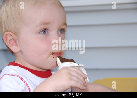 Ein Kleinkind junge isst eine Eis-Sandwich an eine Kinder-Picknick-Tisch draußen in einer Sommernacht. Stockfoto