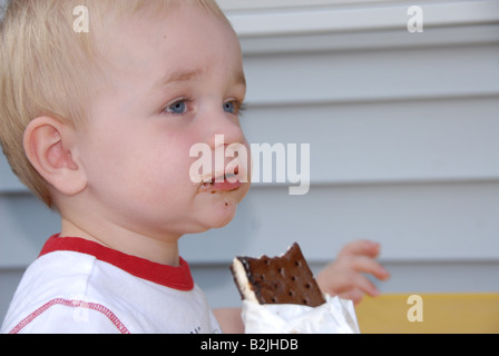 Ein Kleinkind junge isst eine Eis-Sandwich an eine Kinder-Picknick-Tisch draußen in einer Sommernacht. Stockfoto