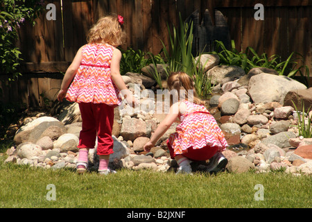 Zwei Zwillinge spielen neben einem Teich im Garten im Sommer Stockfoto