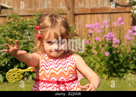 Ein junges Mädchen zu fangen versuchen Seifenblasen auf dem Hof im Sommer Stockfoto