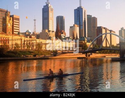 Central Business District reflektiert Yarra River in Melbourne bei Sonnenaufgang mit einem vorbeifahrenden Racing Shell Skiff und Heißluftballon Stockfoto