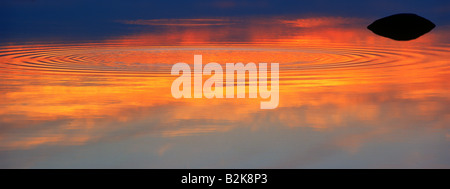 Sonnenuntergang Himmel reflektiert kreisförmige Wellen nach außen auf spiegelglatten Seewasser verteilen Stockfoto