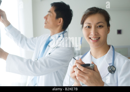 Ärztin, hält eine Daten-Assistent mit einem männlichen Arzt hinter ihr Stockfoto