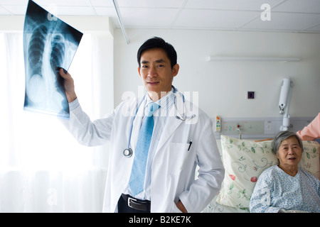 Männlichen Arzt hält einen Röntgen-Bericht mit einem Patienten auf dem Bett Stockfoto