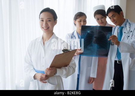 Porträt einer weiblichen Krankenschwester lächelnd mit anderen Ärzten untersuchen einen Röntgen-Bericht im Hintergrund Stockfoto