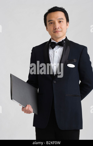 Porträt von Kellner halten ein Menü und stehend mit Hände hinter Rücken Stockfoto