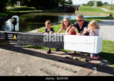 Kinder auf einem Boot Urlaub Push öffnen Schleuse Grand Union Canal England mit Hilfe ihres Vaters Stockfoto