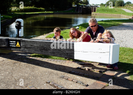 Kinder auf einem Boot Urlaub Push öffnen Schleuse Grand Union Canal England mit Hilfe ihres Vaters Stockfoto