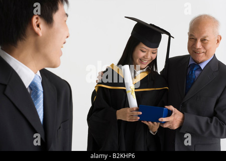 Junge weibliche Absolventin erhält ein Geschenk von ihrem Vater und lächelnd Stockfoto